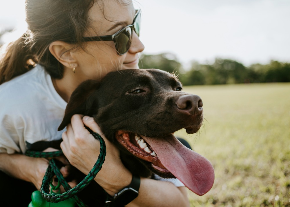 Girl hugging dark-brown dog who has his tongue out